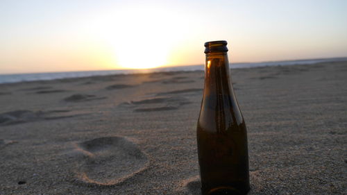 Close-up of beer bottle on beach against sky during sunset