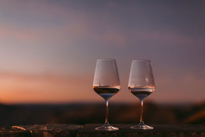 Close-up of wineglass against sky during sunset