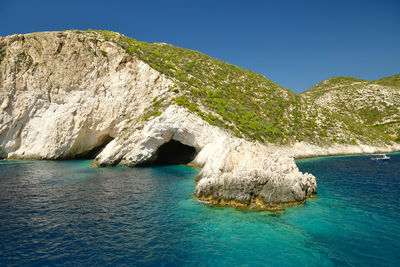 Rock formation in sea against clear blue sky