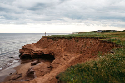 Scenic view of field by sea against cloudy sky