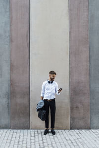Full length of man looking at camera while standing against wall