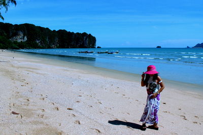 Rear view of woman standing at beach against sky