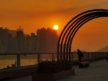 Silhouette man by buildings against sky during sunset