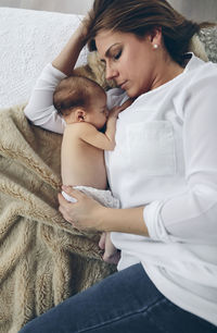 High angle view of mother breastfeeding daughter while lying on bed at home