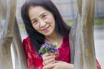 Portrait of smiling woman with pink flowers against tree trunk