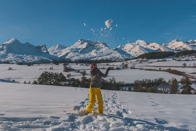 A full-body shot of a young caucasian woman playing with snow in the french alps mountains