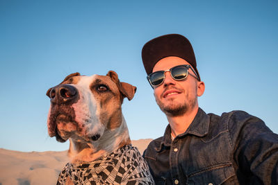 Low angle view of young man sitting with dog against clear sky