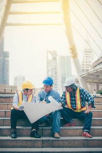 Manual workers discussing over blueprint standing at construction site