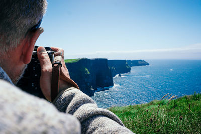 Close-up of man photographing sea against sky