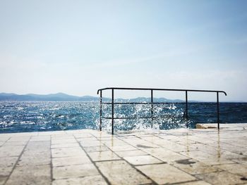 Wave splashing on railing at pier against sky