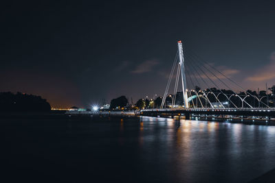 Illuminated bridge over river against sky at night