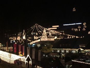 Illuminated city by river against sky at night