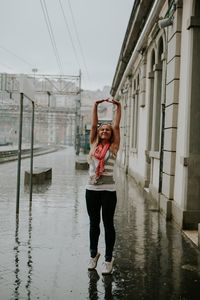 Young woman with arms raised standing at railroad station during rainy season