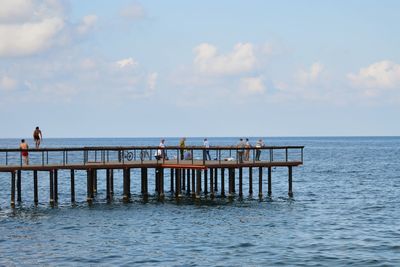 People on pier over sea against sky