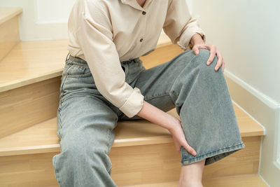 Asian lady woman touch and feel pain her knee on the stairs at home, healthy medical concept.