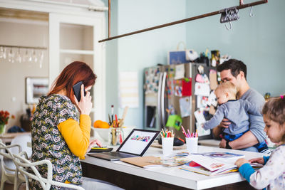 Woman working on laptop while sitting with family in kitchen at home