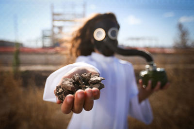 Girl wearing gas mask while holding stones on field