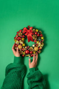 Christmas fir wreath with festive decor in female hands on green background