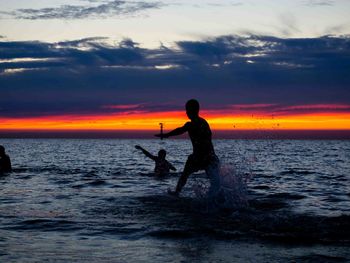 Silhouette men on beach against sky during sunset