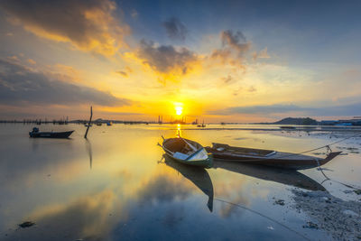 Boats moored in sea against sky during sunset