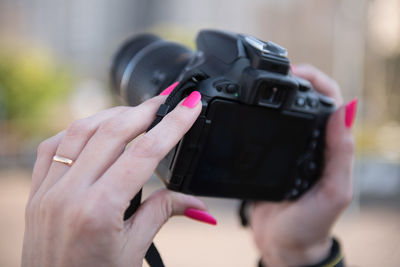 Cropped hand holding camera while standing outdoors