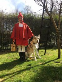 Portrait of happy woman in costume standing with dog on grassy field