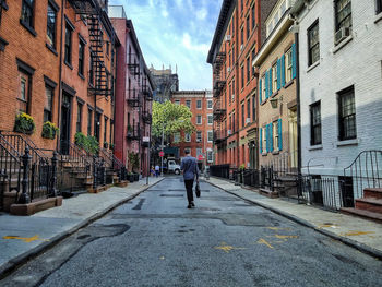 Rear view of man walking on road amidst residential buildings in city