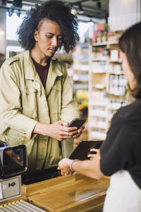 Young male customer scanning through smart phone while paying at checkout counter in store