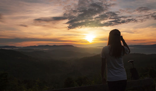 Rear view of woman standing on mountain during sunset