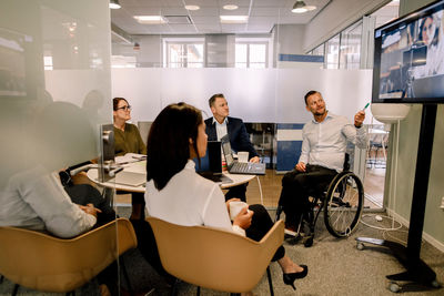 Sales executives video conferencing with female professional during meeting in board room