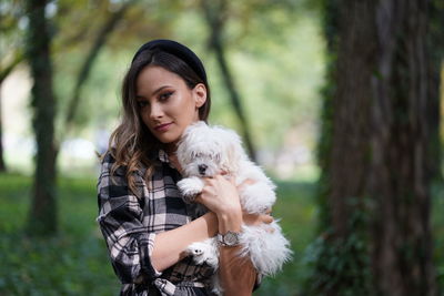 Smiling young woman with dog standing at park