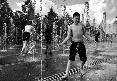 Full length of shirtless boy with arms raised against trees