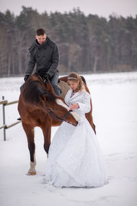 Smiling groom looking at bride touching on snow covered field