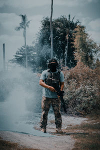 Man with gun airsoft standing on land against sky