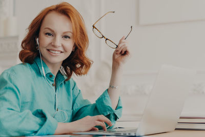 Portrait of smiling young woman using phone while sitting on table