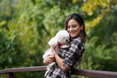 Young smiling woman holding dog standing at park