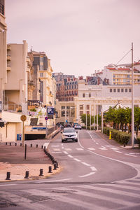 Cars on road by buildings against sky in city