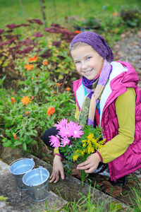 Portrait of smiling girl with pink flowers crouching on grass