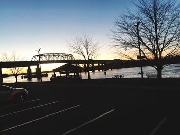 Silhouette bridge over river against sky at sunset