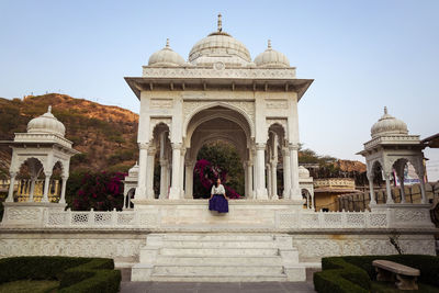 Happy young asian woman smiling and looking away while sitting in aged gaitor ki chhatriyan building in jaipur, india