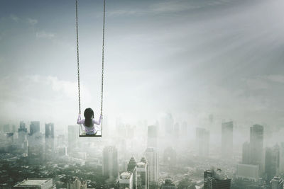 Digital composite image of girl swinging over skyscrapers