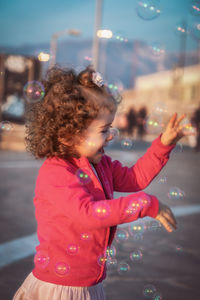 Side view of girl standing amidst bubbles at night