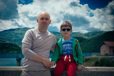 Portrait of father and son on bridge against mountains and sky
