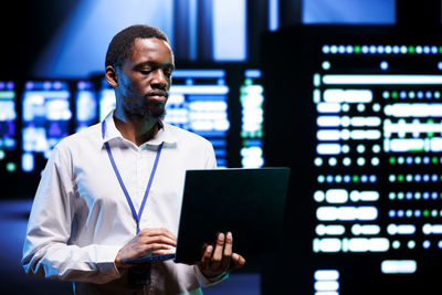 Portrait of young man using laptop while standing in office