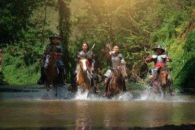 Male warriors riding horses in lake at forest