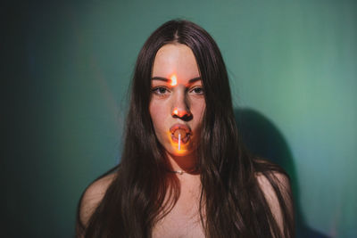 Portrait of beautiful young woman eating lollipop against wall