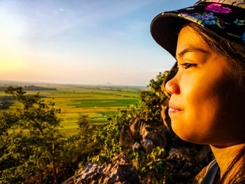 Side view of young woman looking away against sky