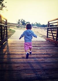 Full length rear view of boy walking on boardwalk