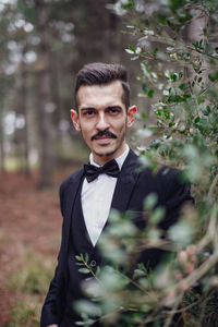 Portrait of young man standing by tree outdoors