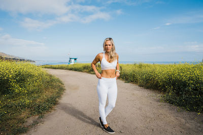 Young woman on dirt path to the beach, surrounded by yellow wildflower